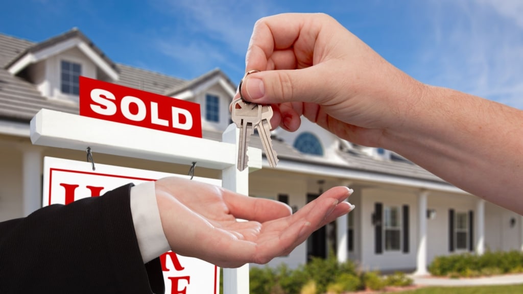 Home keys being handed over in front of a sold sign